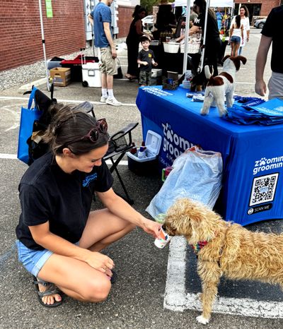 Smiling woman feeding dog water at summer festival in Denver, CO